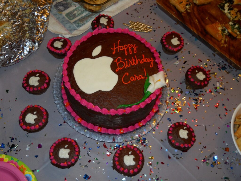 round cake with apple logo and flower surrounded by matching cupcakes