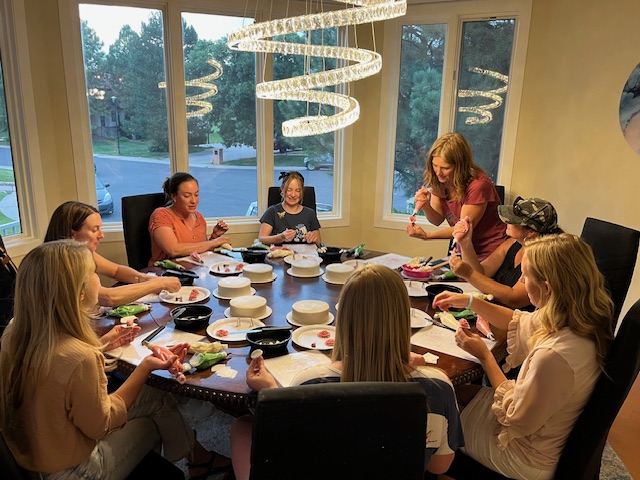 table of women decorating individual cakes with one woman demonstrating