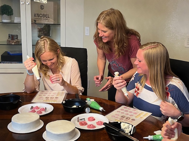 three women laughing while decorating cakes